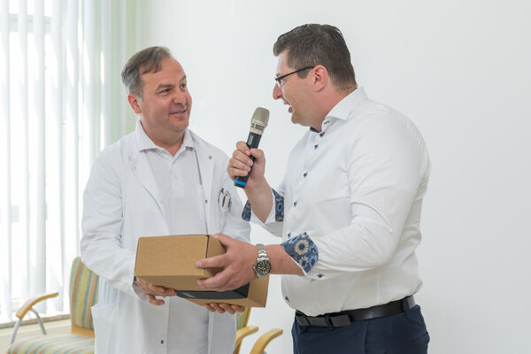 Bild vergr&ouml;&szlig;ern: Das Bild zeigt Landrat Thomas Hennig und den neuen Chefarzt Dr. Leonir Alirifa Sandner. Der Landrat &uuml;berreicht ihm ein Genusspaket und spricht dabei ins Mikrofon.