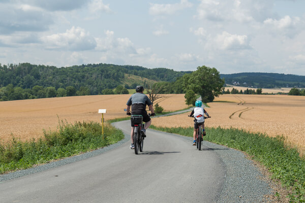Bild vergr&ouml;&szlig;ern: Das Bild zeigt zwei Radfahrer auf einem asphaltierten Radweg. Im Hintergrund sind Felder zu sehen.