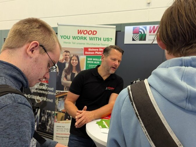 Zwei junge M&auml;nner stehen vor einem Stand vor Wurzbacher.