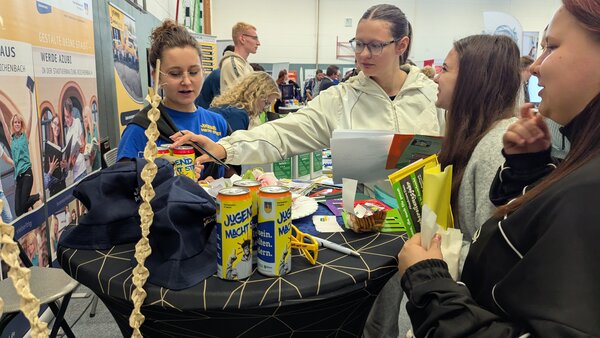 Bild vergr&ouml;&szlig;ern: Vier junge Frauen stehen am Stand der Stadtverwaltung Reichenbach und sehen sich die Merchandiseartikel an.
