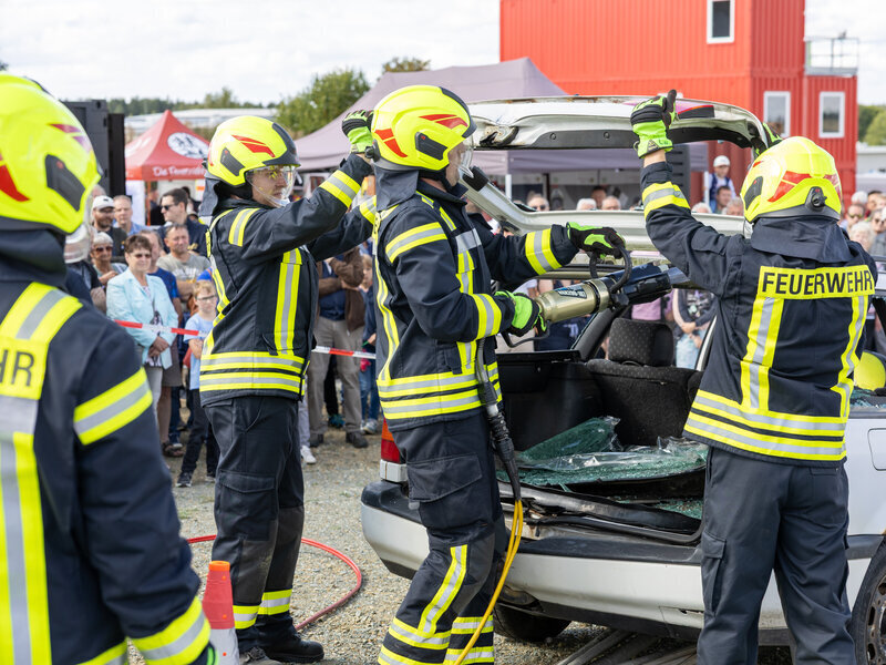 Feuerwehrleute nehmen mit schwerem Ger&auml;t ein altes Auto auseinander. Sie haben die Heckscheibe entfernt.