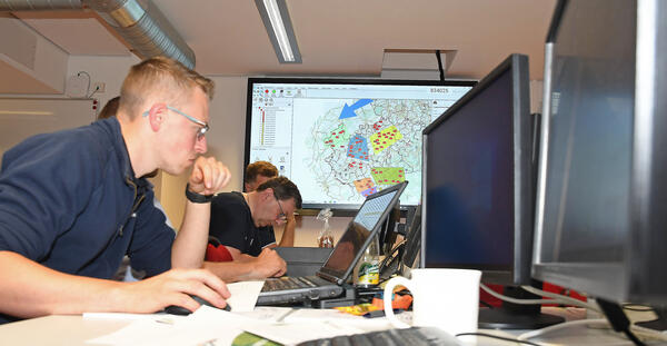 Bild vergr&ouml;&szlig;ern: Das Bild zeigt Teilnehmer der �bung des Brand- und Katastrophenschutzes bei konzentriertem Arbeiten an ihren Computern. Im Hintergrund befindet sich eine Karte des Vogtlandkreises.