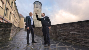 Bild vergr&ouml;&szlig;ern: Das Bild zeigt den Beigeordneten Dr. Axel Steinbach  und Archiv-Leiter Dr. Christian Espig auf dem historischen Au&szlig;engel&auml;nde von Schloss Voigtsberg. Man sieht einen alten, steinernen Weg mitsamt einer historischen Schlossmauer. Im Hintergrund den Schlossturm.