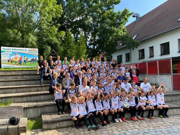 Bild vergr&ouml;&szlig;ern: Das Bild zeigt die Teilnehmerinnen und Teilnehmer der Sparkasse Vogtland Fu�ballschule auf einer Treppe sitzend. Sie alle tragen wei�e Trikots und Fu�ballschuhe.