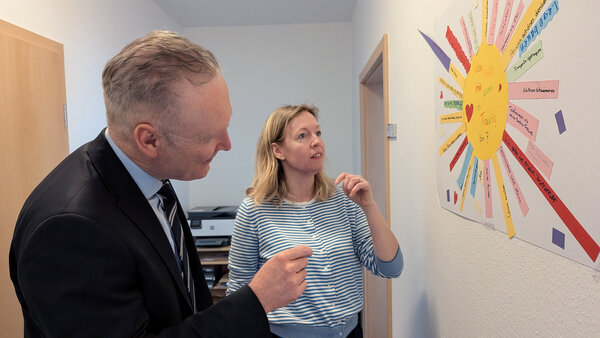 Bild vergr&ouml;&szlig;ern: Dr. Steinbach schaut auf eine Plakatwand. Darauf ist eine gebastelte Sonne zu sehen.