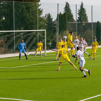 Bild vergr&ouml;&szlig;ern: Fu&szlig;ballspiel auf einem Kunstrasenplatz: Mehrere Spieler in gelben und wei&szlig;en Trikots springen im Strafraum zum Kopfball. Ein Torwart steht vor dem Tor bereit.