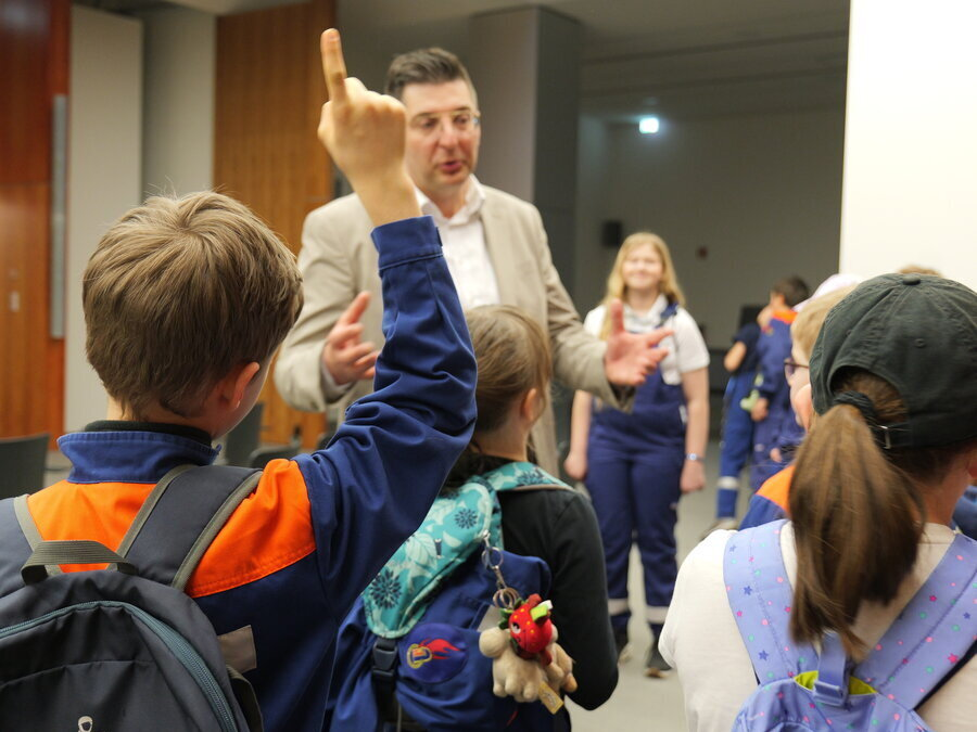 Landrat Thomas Hennig spricht vor den Kindern im Kreistagssaal. Ein Kind hat eine Frage und meldet sich.