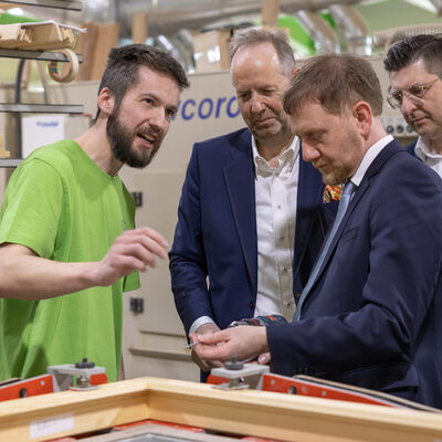 Bild vergr&ouml;&szlig;ern: W&auml;hrend des Rundgangs erl&auml;utert ein Mitarbeiter in der Werkhalle die Fertigung eines Holzfensters. Die Besucher verfolgen die Erkl&auml;rung direkt am Werkst&uuml;ck.
