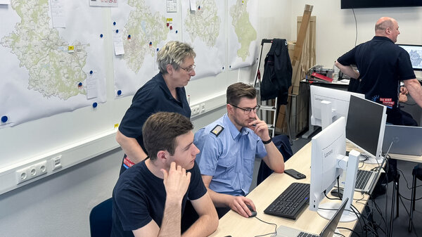 Bild vergr&ouml;&szlig;ern: Mitglieder der F�hrungsgruppe sitzen an einem Rechner, hinter ihnen zahlreiche Karten.