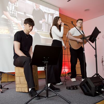 Bild vergr&ouml;&szlig;ern: Drei junge Musikerinnen und Musiker stehen bei der AWO-Festveranstaltung auf einer B&uuml;hne mit Mikrofon, Gitarre und Caj&oacute;n.