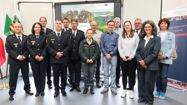 Bild vergr&ouml;&szlig;ern: Mitglieder des Brandschutzes Tschechien und Vogtland haben f�r ein Gruppenfoto im Tagungsraum Aufstellung genommen. Sie tragen meist Uniform und Funktionskleidung.