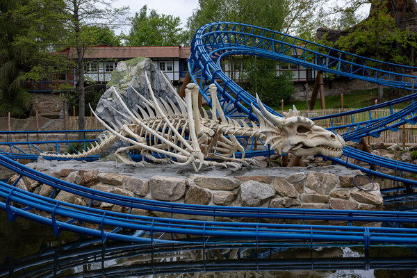 Bild vergr&ouml;&szlig;ern: Gro&szlig;es wei&szlig;es Drachenskelett auf Steinsockel zwischen den blauen Schienen der Achterbahn &raquo;D&oslash;nnervind" im Freizeitpark Plohn.