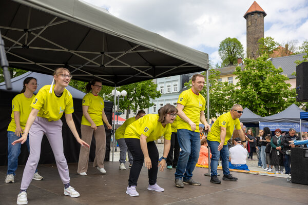 Bild vergr&ouml;&szlig;ern: Eine inklusive Tanzgruppe in gelben T-Shirts tritt auf der B&uuml;hne des Auerbacher Familientages auf; im Hintergrund sind Besucher und der Schlossturm zu sehen