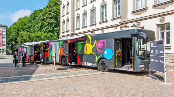 Bild vergr&ouml;&szlig;ern: Das Bild zeigt den bunt gestalteten Suchtpr&auml;ventionsbus, der den Namen "TraumRausch" tr&auml;gt. Er ist dunkelgrau und wurde mit bunten gro&szlig;en Blasen beklebt.