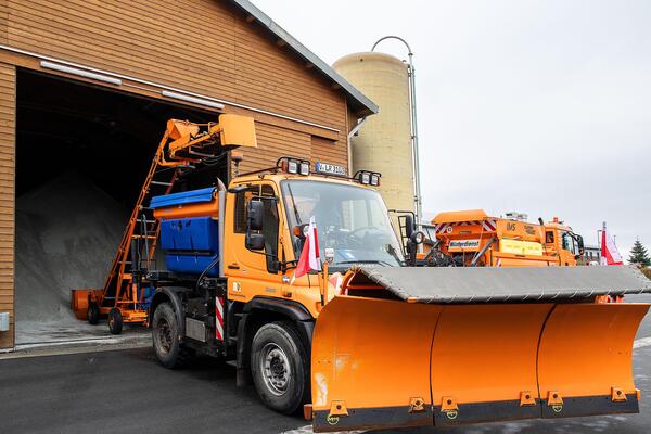 Bild vergr&ouml;&szlig;ern: Das Bild zeigt einen orange-farbenen Schneepflug vor der Einfahrt einer Halle, in der Streusalz f�r den Winterdienst gelagert wird.