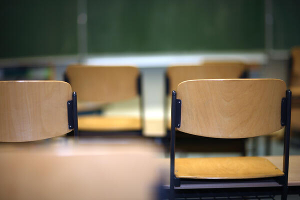 Bild vergr&ouml;&szlig;ern: Das Bild zeigt ein typisches Klassenzimmer. Die Holzst�hle sind auf die Schulb�nke gestellt - im Hintergrund befindet sich eine gr�ne Tafel.