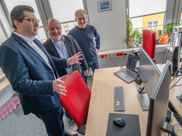 Bild vergr&ouml;&szlig;ern: Drei M&auml;nner stehen am Schreibtisch